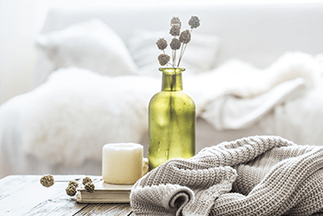 Green vase with dried flowers, a candle, and knitted blanket on table in cozy room