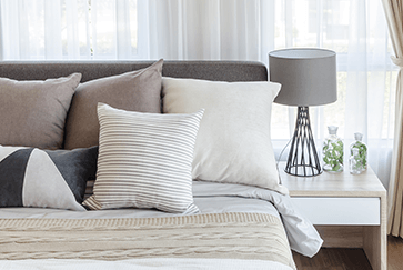 modern bedroom with neutral tones featuring pillows, bedside table, and a stylish lamp