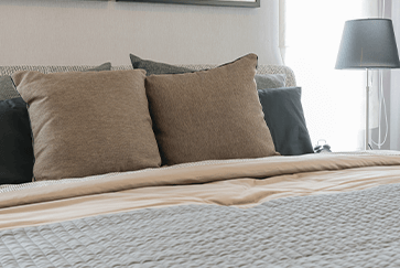 A neatly made bed with brown and black pillows beside a small table lamp in a cozy bedroom.