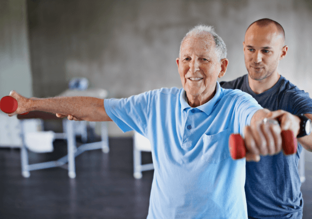 Senior man lifting hand weights with the help of a therapist