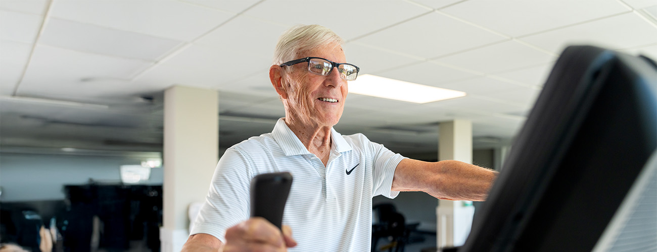 Smiling senior man exercising on a treadmill in a well-lit fitness room.