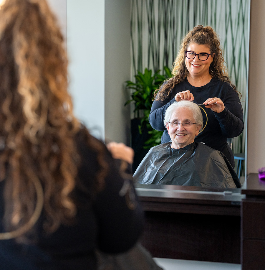 Smiling elderly resident receives a haircut from a stylist in a community salon.