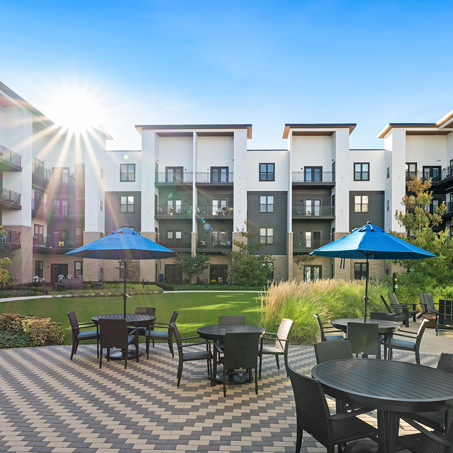 Modern building with outdoor seating and blue umbrellas in a landscaped courtyard.