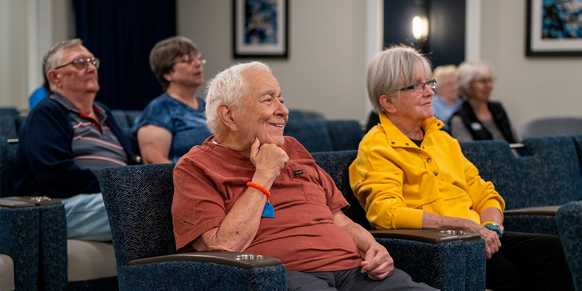 Seniors engaged in a group activity within a communal setting, seated and attentive.