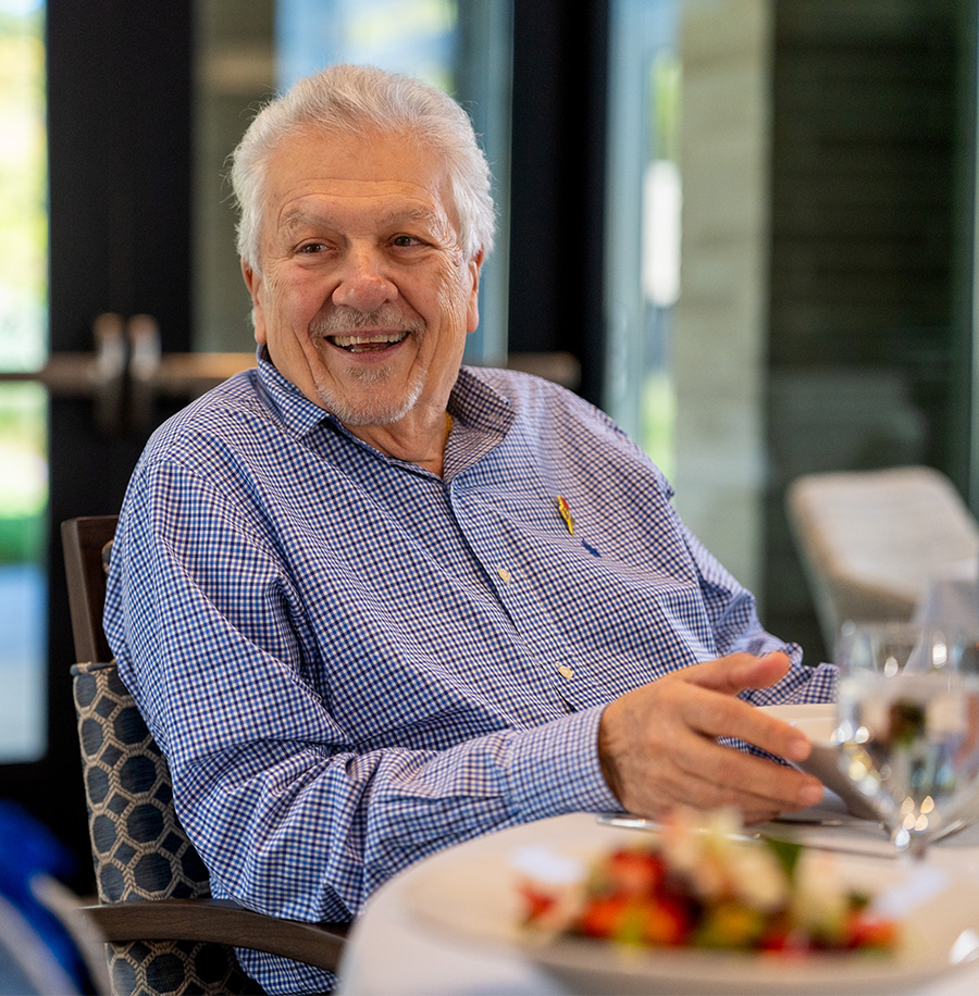 Smiling elderly man dining at a table in a bright community dining room.