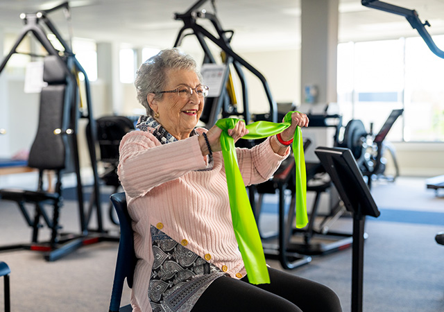 Elderly woman exercising with resistance band in community fitness room.