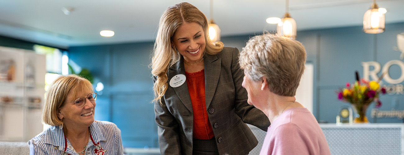 Warm Interaction in Community Lobby Friendly staff member conversing with two smiling residents in a welcoming lobby area.