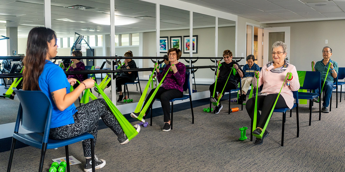 Residents participating in a seated exercise with resistance bands in a fitness room.