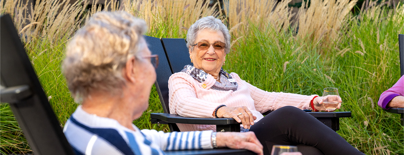 Relaxing in Community Garden Two elderly women enjoying outdoor seating in garden area.