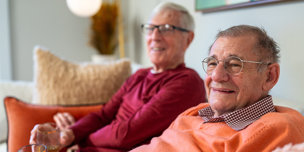 Two senior men smiling and relaxing in a comfortable indoor setting.