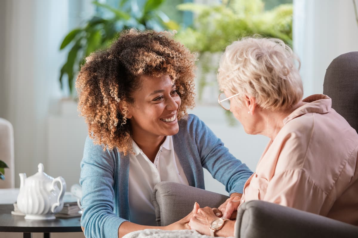 Young adult nurse smiling at seated senior woman